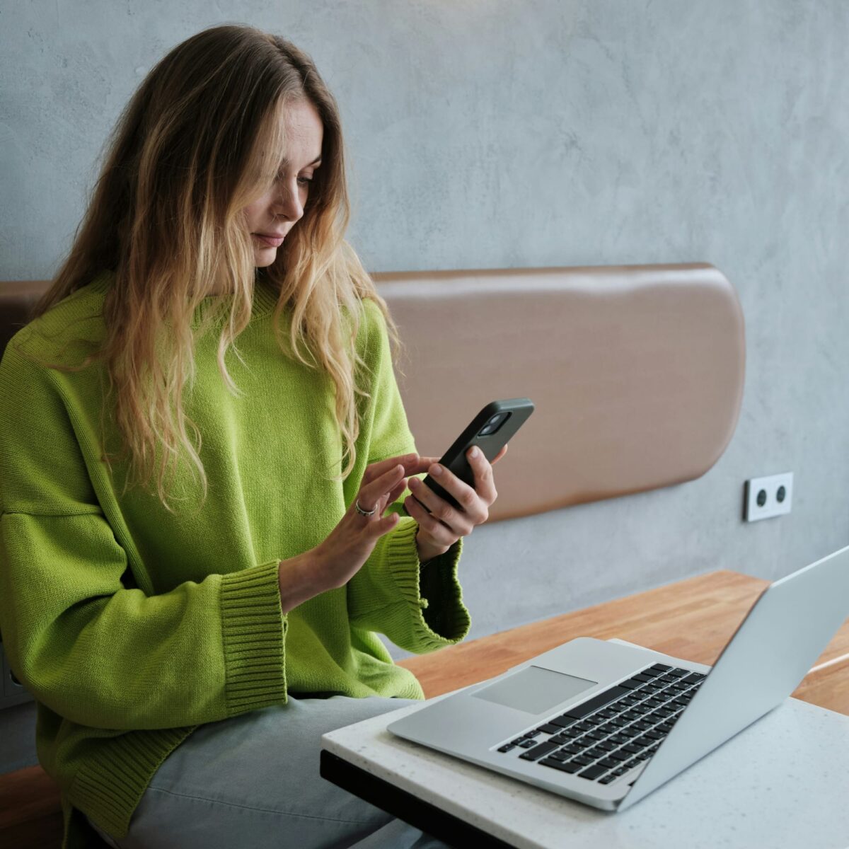 A woman in a green sweatshirt is holding a phone and looking at the screen